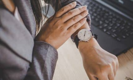 Blick auf Armbanduhr vor Laptop Vollzeit arbeiten