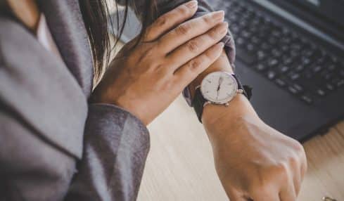 Blick auf Armbanduhr vor Laptop Vollzeit arbeiten