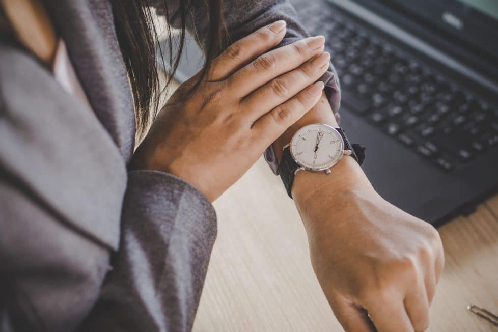 Blick auf Armbanduhr vor Laptop Vollzeit arbeiten