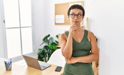 Eine kurzhaarige Frau mit einem engnaliegenden, olivengrünen Kleid denkt über ihr Sommer Büro Outfit nach