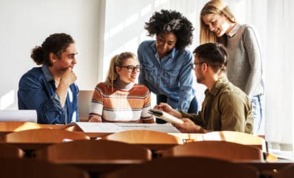 Fünf Arbeitskollegen unterhalten sich am Tisch über Berufe in der Erwachsenenbildung