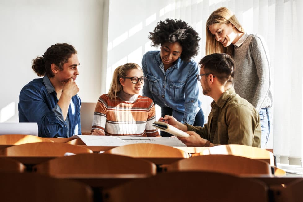 Fünf Arbeitskollegen unterhalten sich am Tisch über Berufe in der Erwachsenenbildung