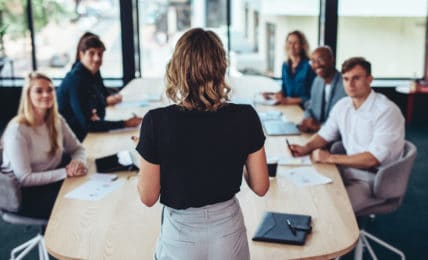 Eine Business-Frau überzeugt bei einem Meeting ihre Kollegen durch ihr sicheres Auftreten.