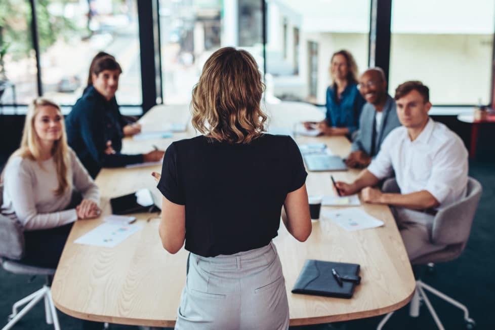 Eine Business-Frau überzeugt bei einem Meeting ihre Kollegen durch ihr sicheres Auftreten.