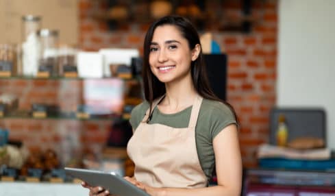 Junge Mitarbeiterin im Café mit Laptop freut sich über neue Verdienstgrenze im Minijob