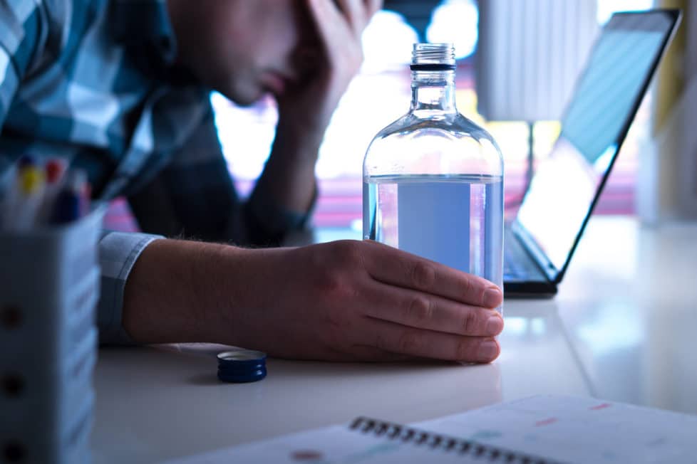 Alkohol am Arbeitsplatz Mann sitzt mit Wodkaflasche in der Hand vor Laptop