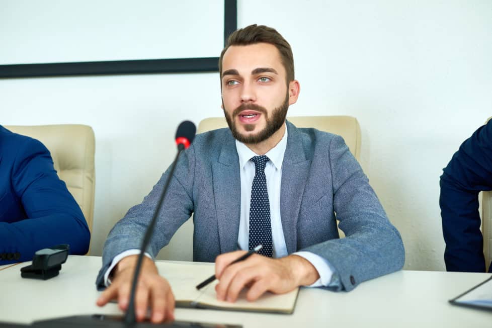 Junger Bürgermeister hält politische Rede sitzend vor Mikrofon